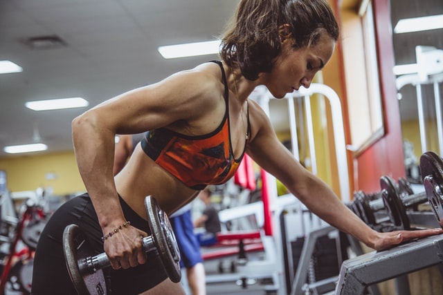 girl in gym doing a dumbbell row as part of a strength workout, exercises for beginners just starting their fitness journey