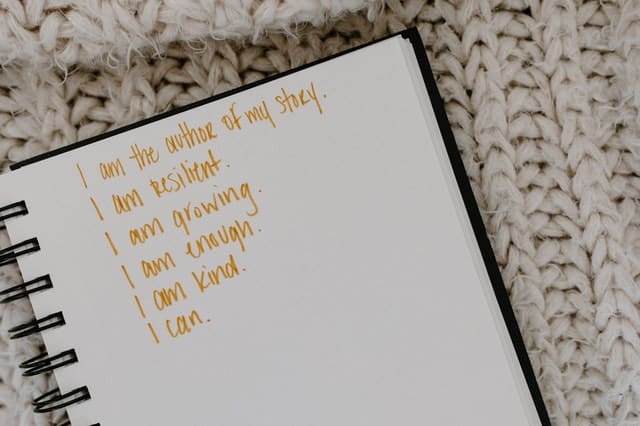 notebook on blanket that reads "I am the author of my story. I am resilient. I am growing. I am enough. I am kind. I can."