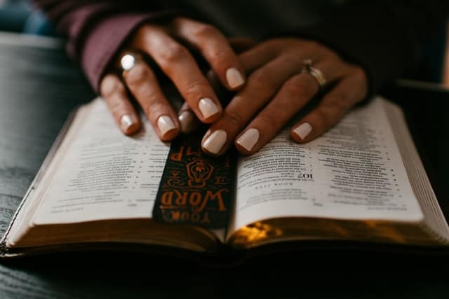 hands resting on open bible with bookmark