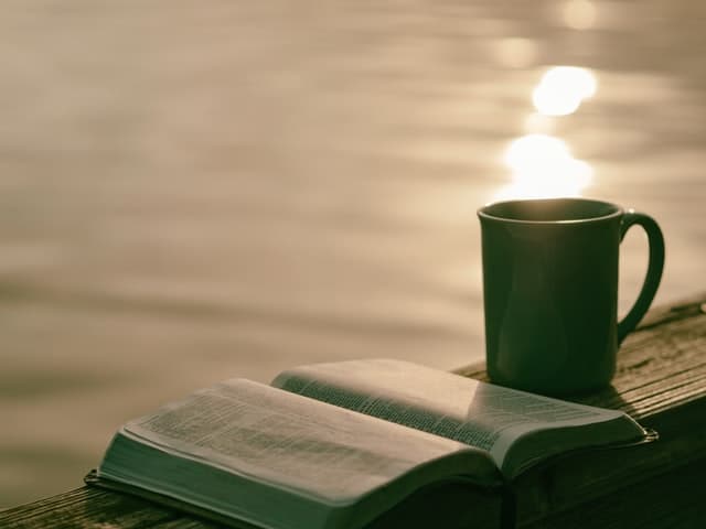 open bible and mug on ledge by water