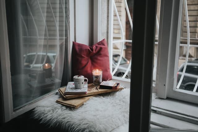 window in corner with pillow, candle, drink, and notebook