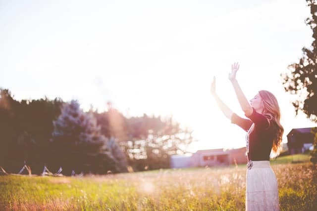 woman outside in sun with hands raised and eyes closed