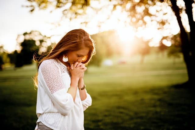 woman outside in the sun with hands clasped and head bowed in prayer