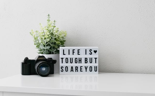 desk with camera, plant, and sign that reads "life is tough but so are you"