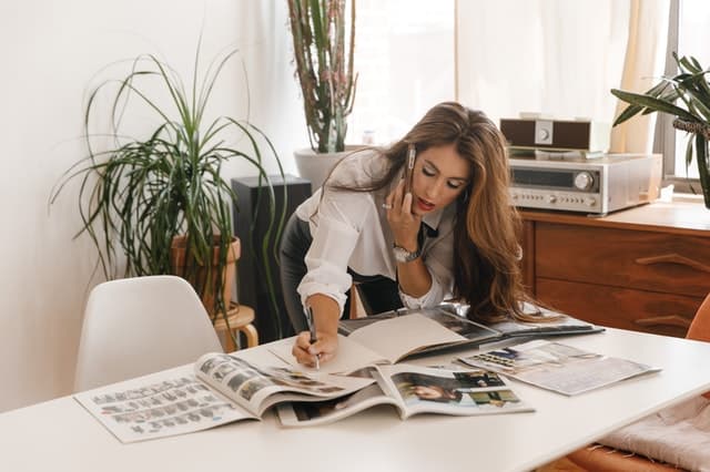 woman on the phone, leaning over a desk writing in a notebook