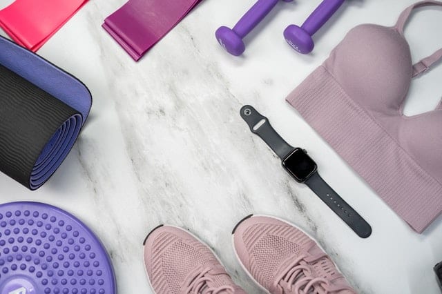 workout equipment on the floor- dumbbells, sports bra, watch, sneakers, yoga mat, and exercise bands