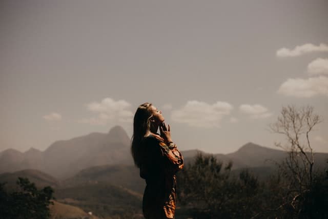 woman outside with hands folded and head looking toward sky in worship