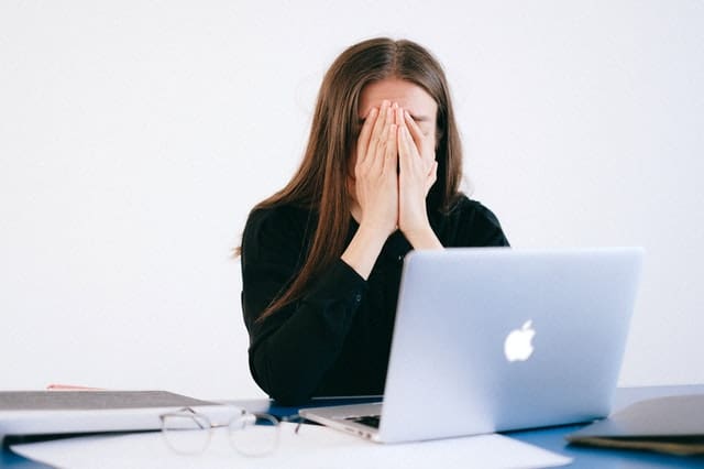 woman sitting at laptop with hands over her face feeling anxiety